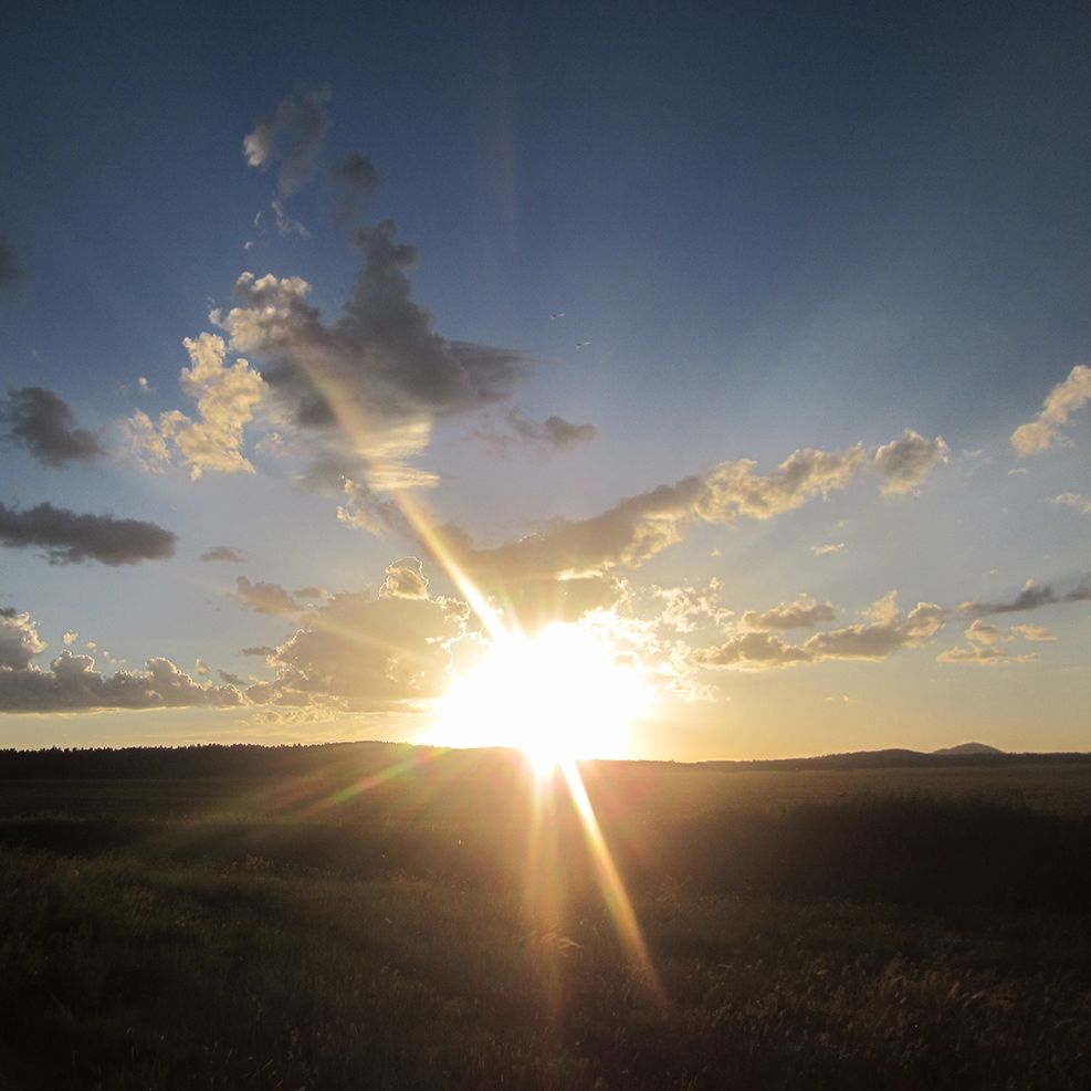 Emerging Light by Usha Lamat, a landscape photograph of the sun rising or setting over a dark horizon with radiant beams and scattered clouds